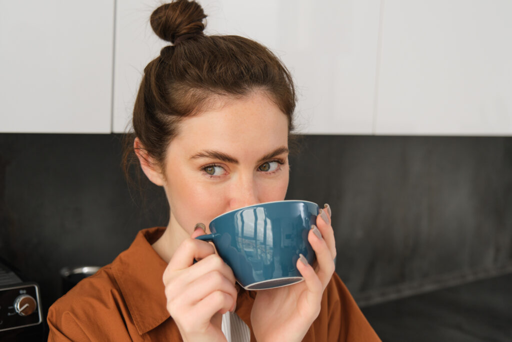 Young woman enjoying aroma of coffee, drinking decaf coffee and smiling. 