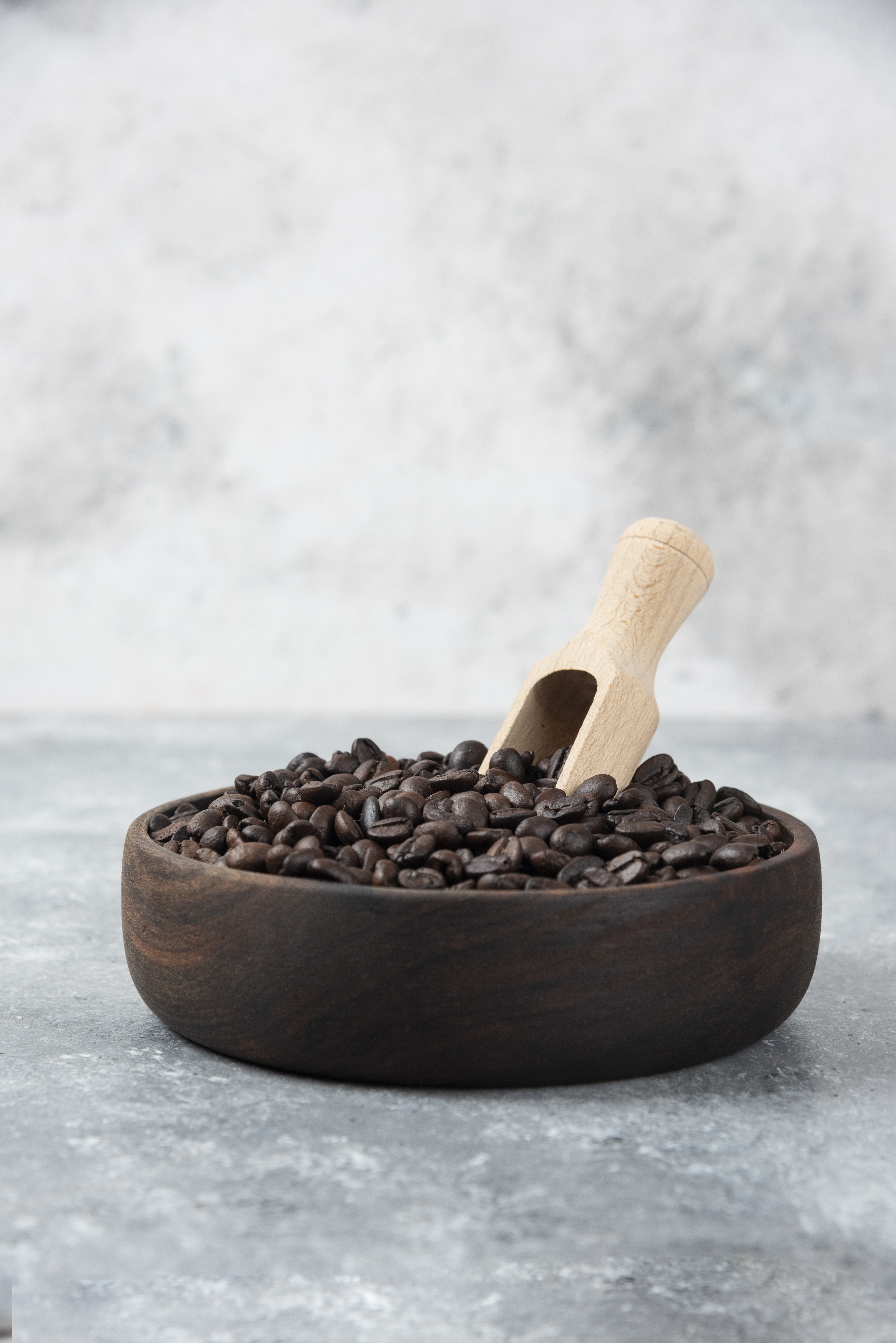 Wooden bowl of medium roasted coffee with spoon on marble surface. 